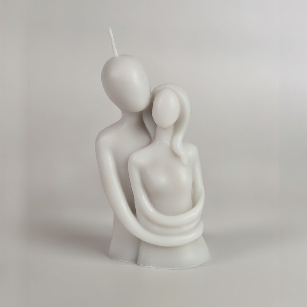 Grey candle sculpture of two people embracing on a plain background