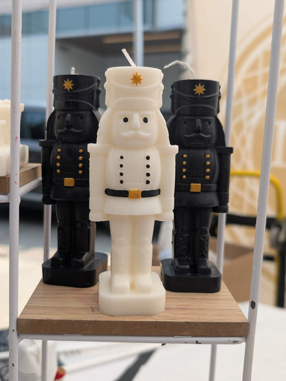 Three Nutcracker-shaped candles on a wooden platform with a blurred background