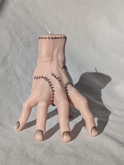 Candle shaped like a hand with stitches on a gray surface