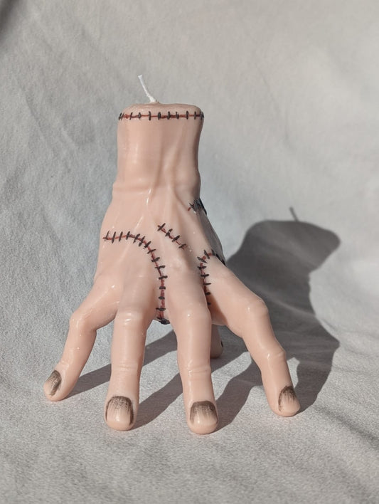 Candle shaped like a hand with stitches on a gray surface