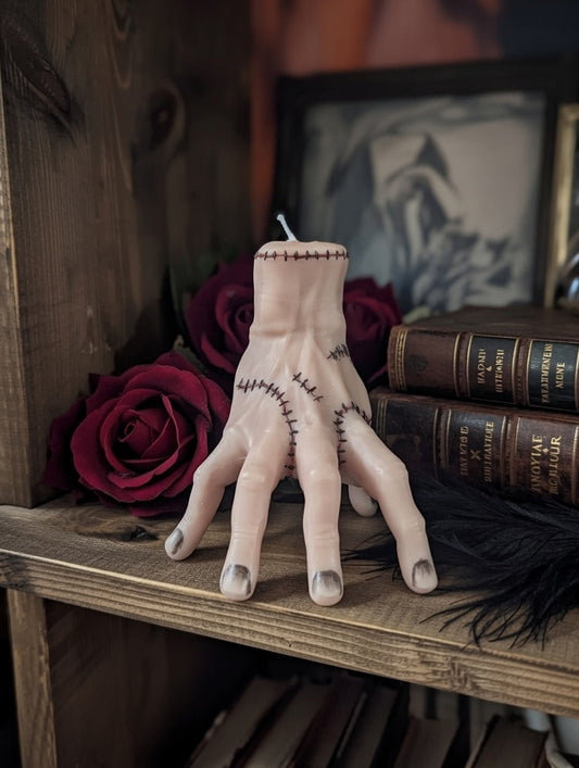 "Thing"-shaped candle with stitches on a wooden shelf with books and roses