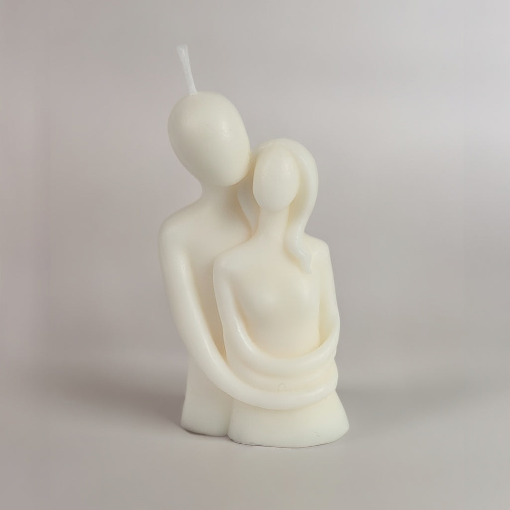 White candle shaped like two people embracing on a plain background